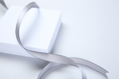 Photo of Beautiful grey ribbon and gift box on white background, space for text