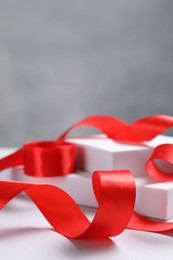 Photo of Beautiful red ribbon and gift boxes on white table