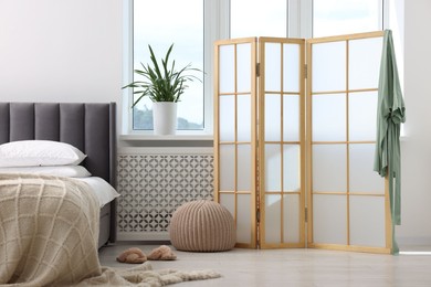 Photo of Folding screen, pouffe, bed and houseplant in bedroom