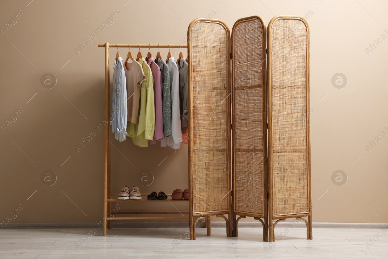 Photo of Folding screen and clothing rack with clothes near beige wall indoors