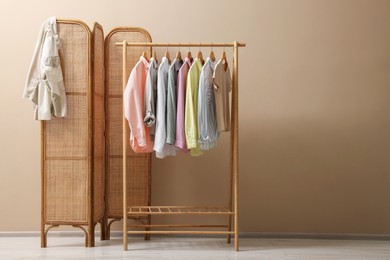 Photo of Folding screen and clothing rack with clothes near beige wall indoors, space for text