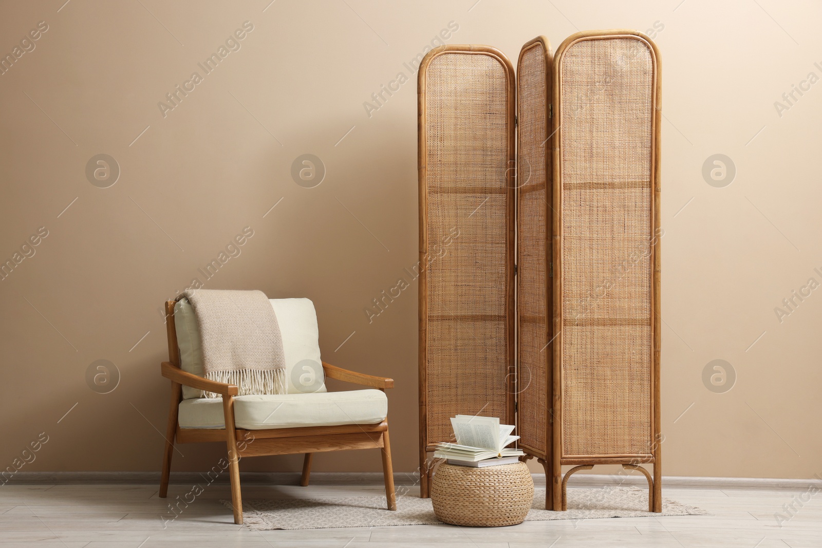 Photo of Folding screen, armchair and blanket near beige wall indoors