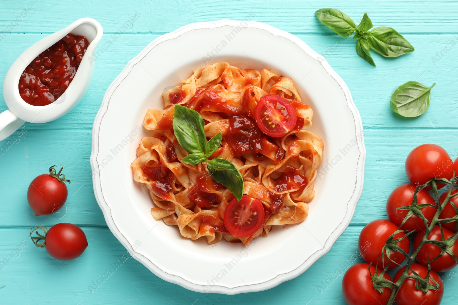 Photo of Delicious pasta with tomato sauce and basil on turquoise wooden table, flat lay