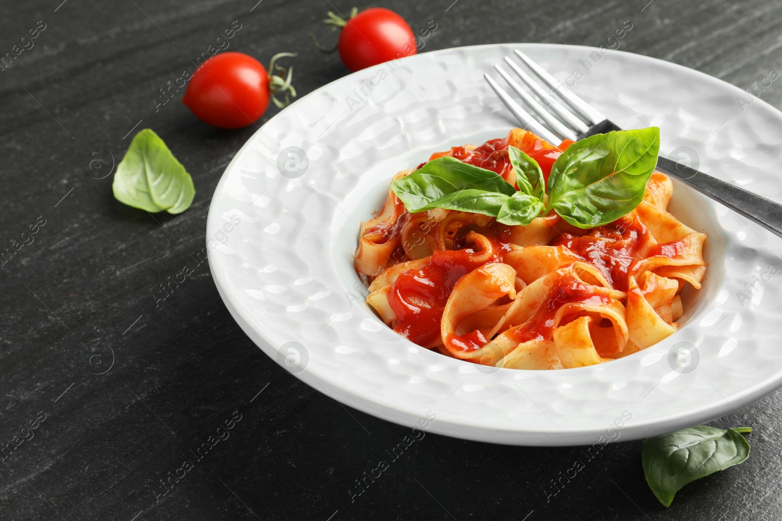 Photo of Delicious pasta with tomato sauce and basil on dark textured table, closeup