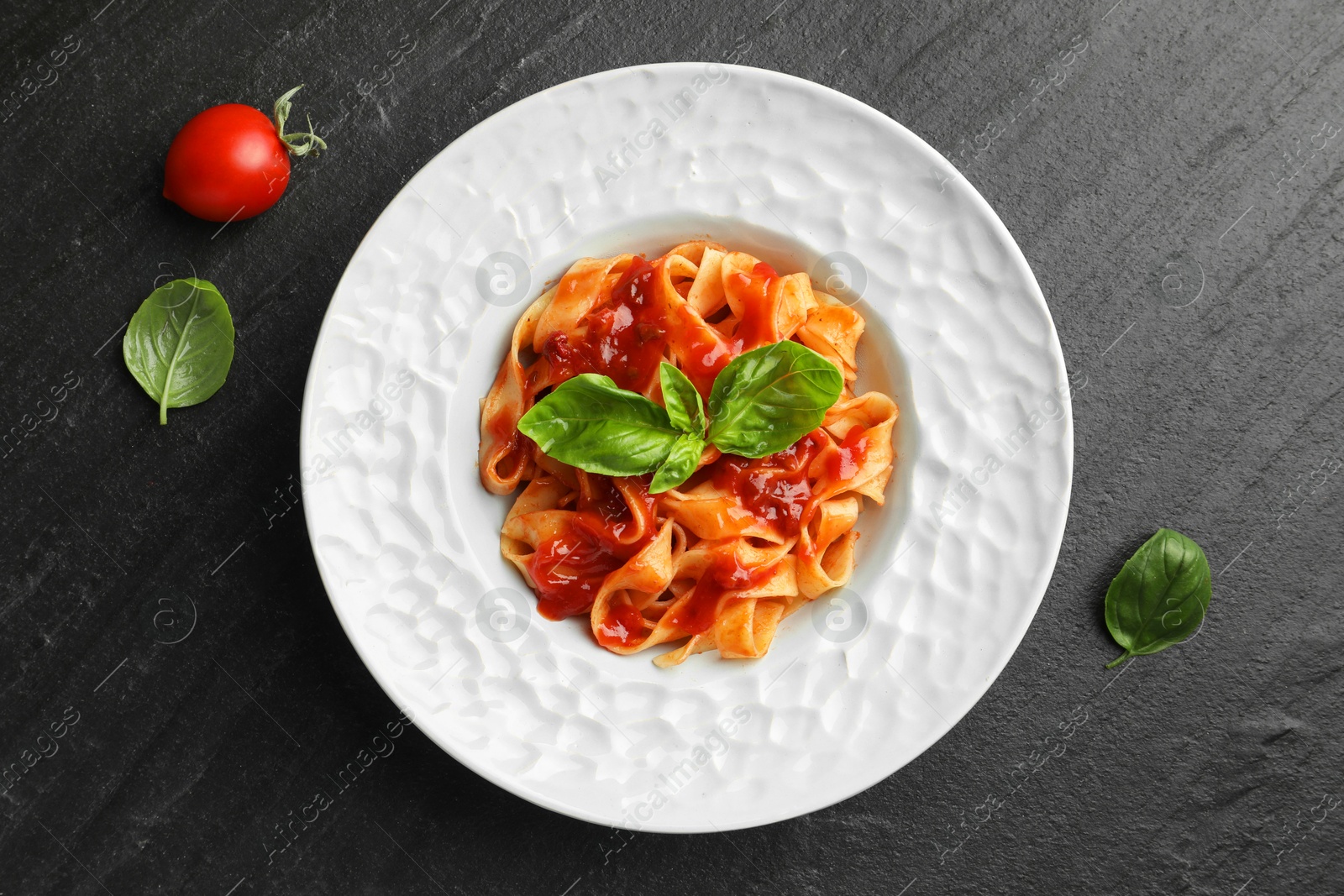 Photo of Delicious pasta with tomato sauce and basil on dark textured table, flat lay