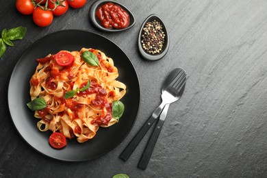 Photo of Delicious pasta with tomato sauce, vegetable, basil and spices served on dark textured table, flat lay. Space for text