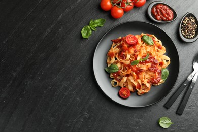 Photo of Delicious pasta with tomato sauce, vegetable, basil and spices served on dark textured table, flat lay. Space for text