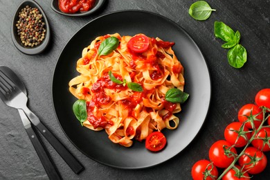 Photo of Delicious pasta with tomato sauce, vegetable, basil and spices served on dark textured table, flat lay