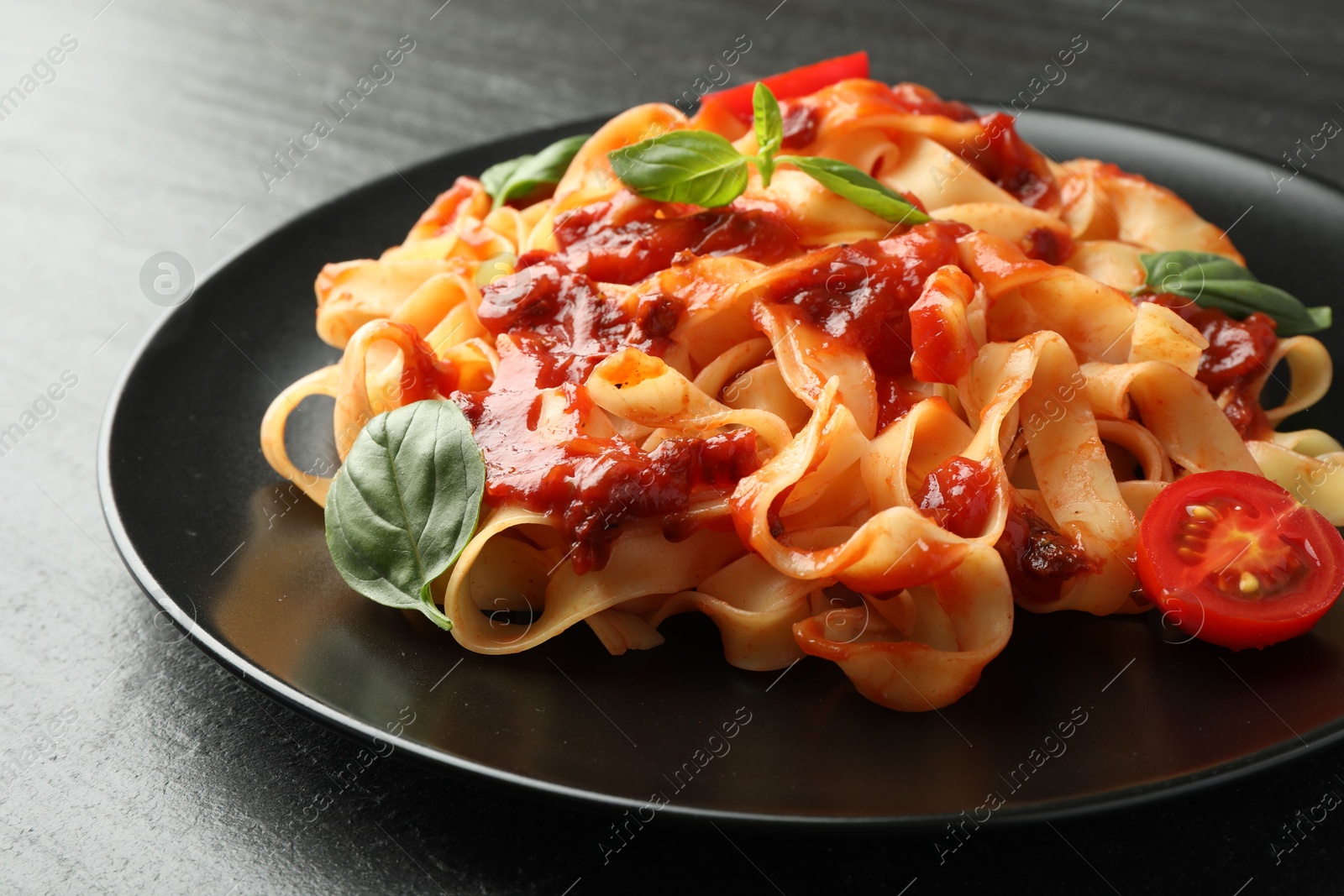 Photo of Delicious pasta with tomato sauce, vegetable and basil on dark textured table, closeup