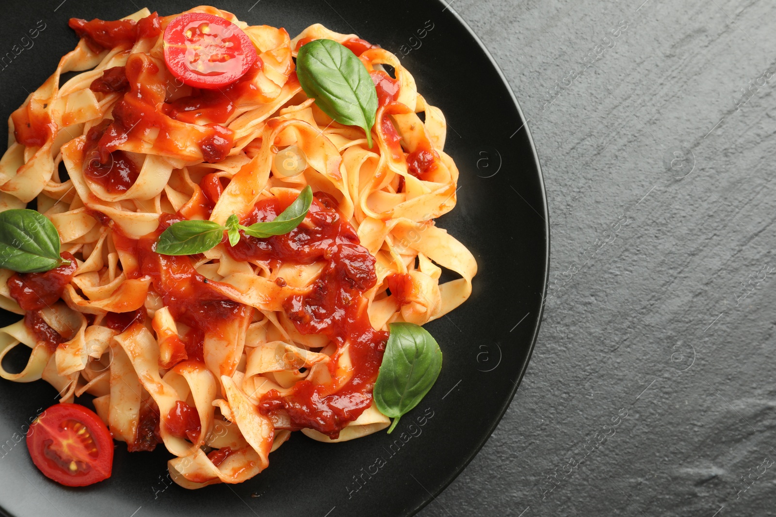 Photo of Delicious pasta with tomato sauce, vegetable and basil on dark textured table, top view. Space for text