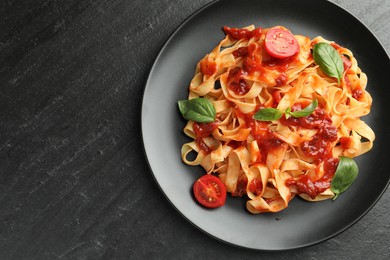 Photo of Delicious pasta with tomato sauce, vegetable and basil on dark textured table, top view. Space for text