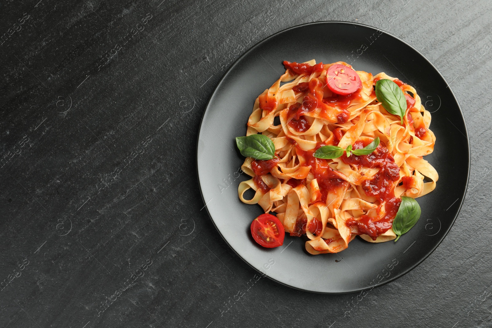 Photo of Delicious pasta with tomato sauce, vegetable and basil on dark textured table, top view. Space for text