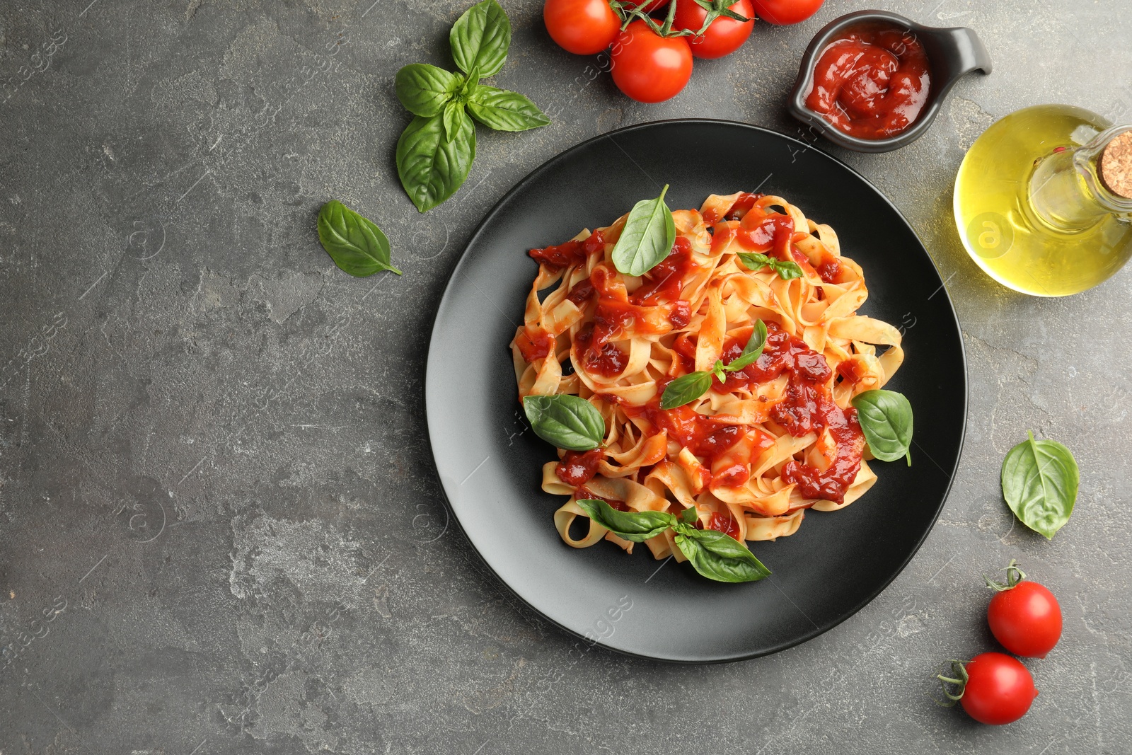 Photo of Delicious pasta with tomato sauce, basil and products on grey textured table, flat lay. Space for text