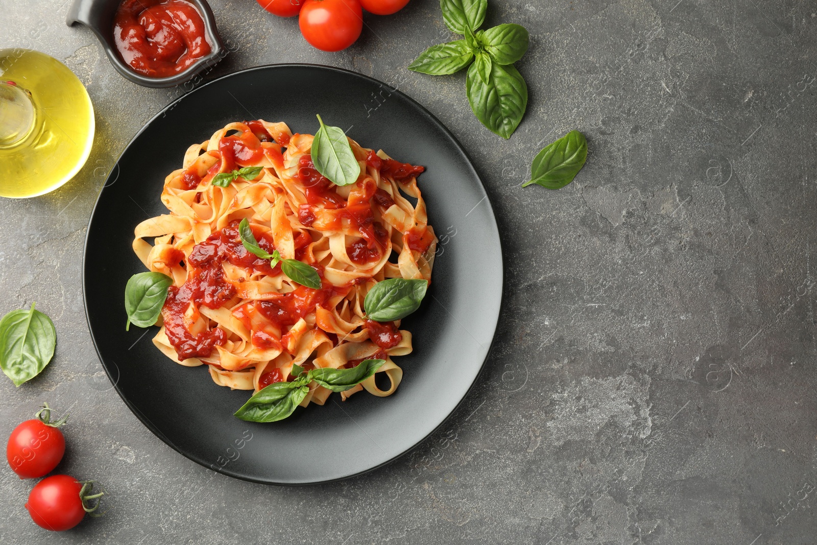 Photo of Delicious pasta with tomato sauce, basil and products on grey textured table, flat lay. Space for text