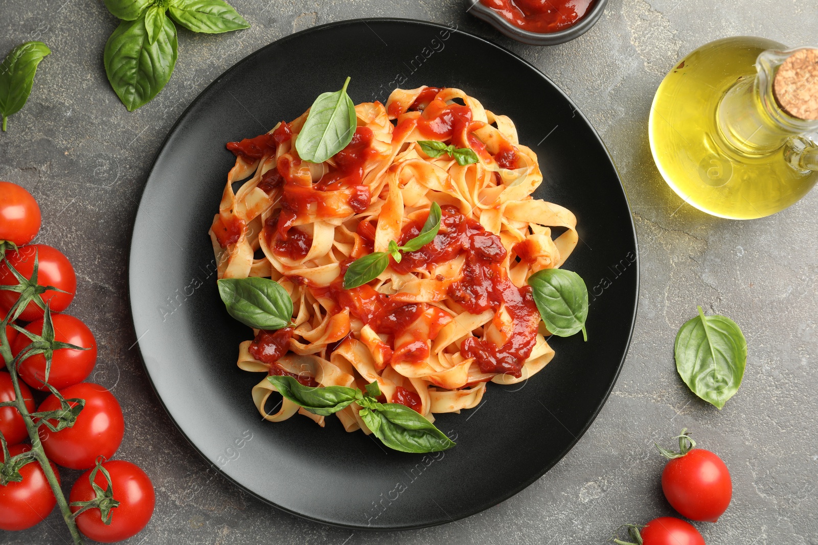 Photo of Delicious pasta with tomato sauce, basil and products on grey textured table, flat lay