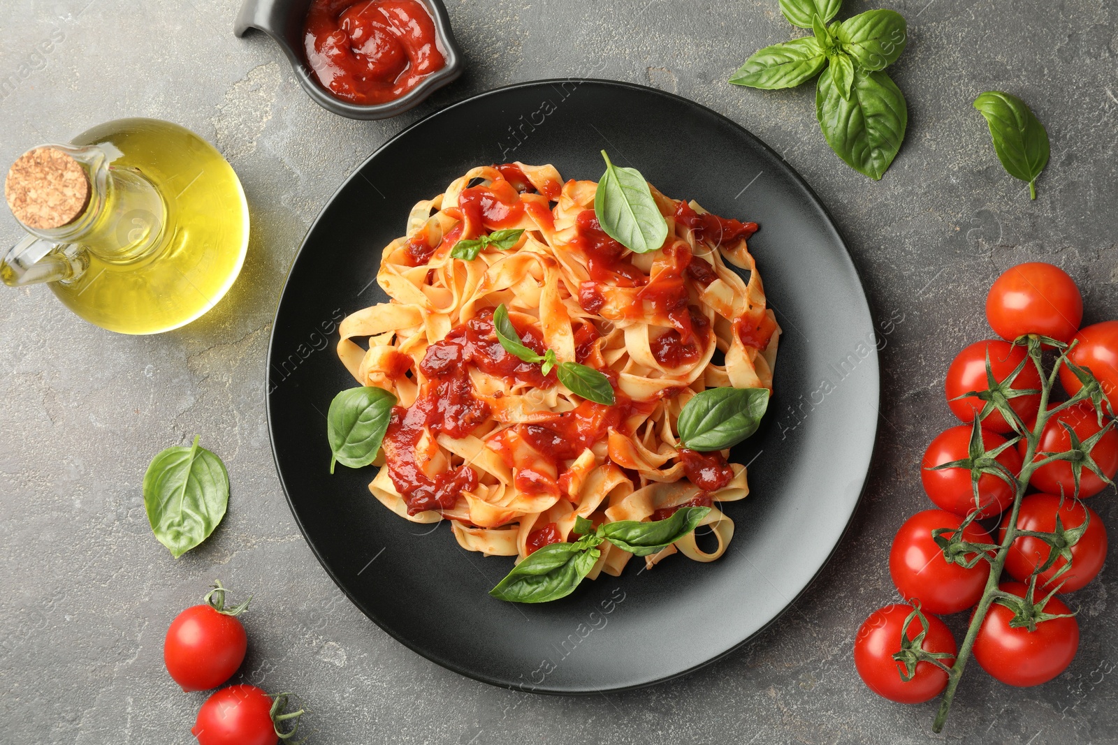 Photo of Delicious pasta with tomato sauce, basil and products on grey textured table, flat lay