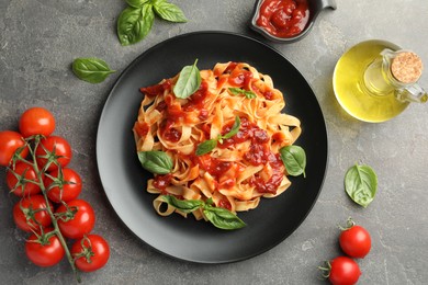 Photo of Delicious pasta with tomato sauce, basil and products on grey textured table, flat lay