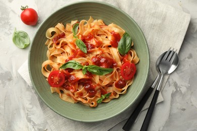 Delicious pasta with tomato sauce and basil served on grey textured table, flat lay