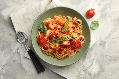 Photo of Delicious pasta with tomato sauce and basil served on grey textured table, flat lay