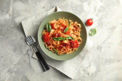 Delicious pasta with tomato sauce and basil served on grey textured table, flat lay