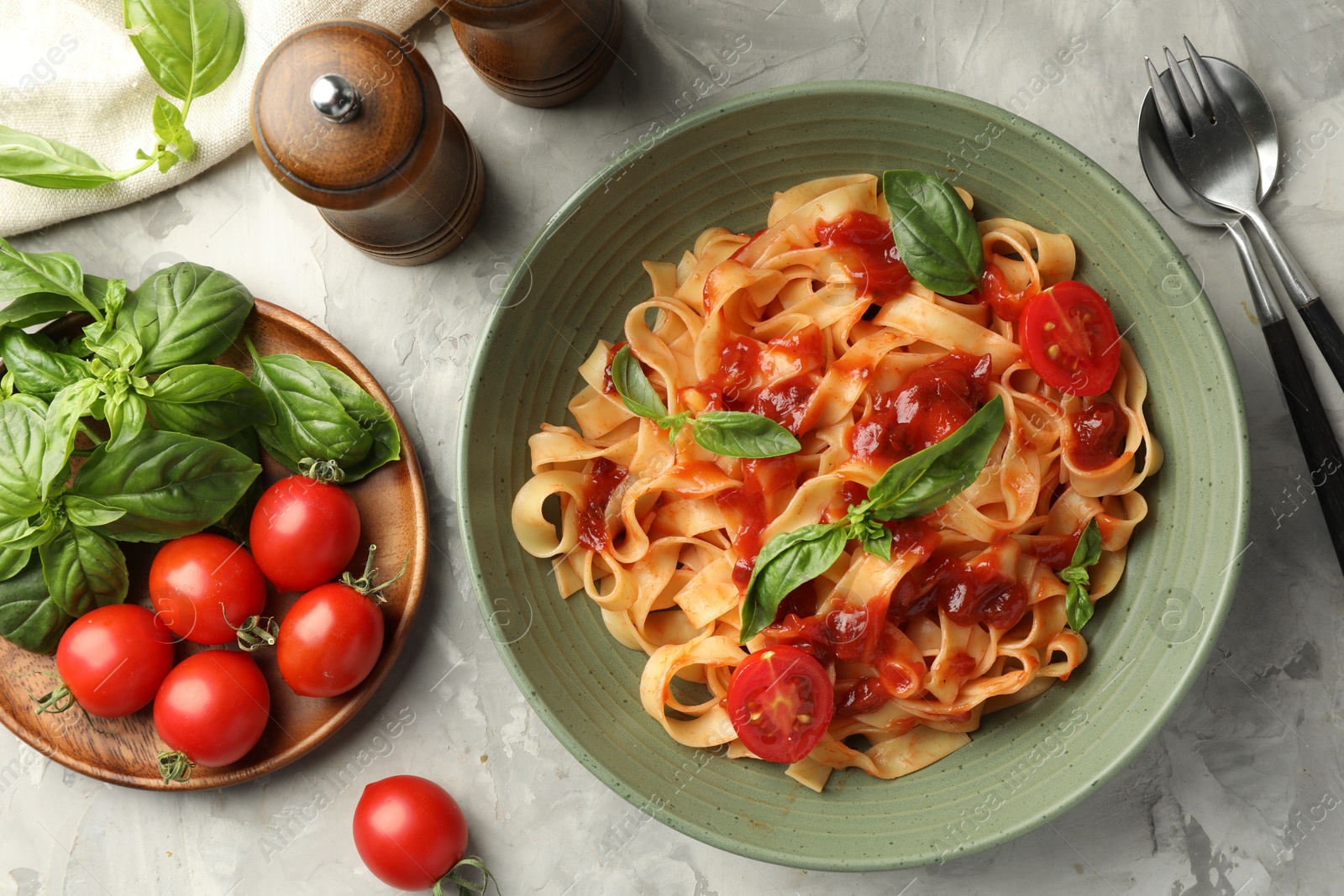 Photo of Delicious pasta with tomato sauce and basil served on grey textured table, flat lay