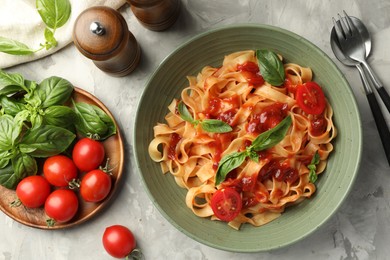 Delicious pasta with tomato sauce and basil served on grey textured table, flat lay