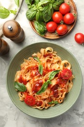 Photo of Delicious pasta with tomato sauce and basil in bowl on grey textured table, flat lay