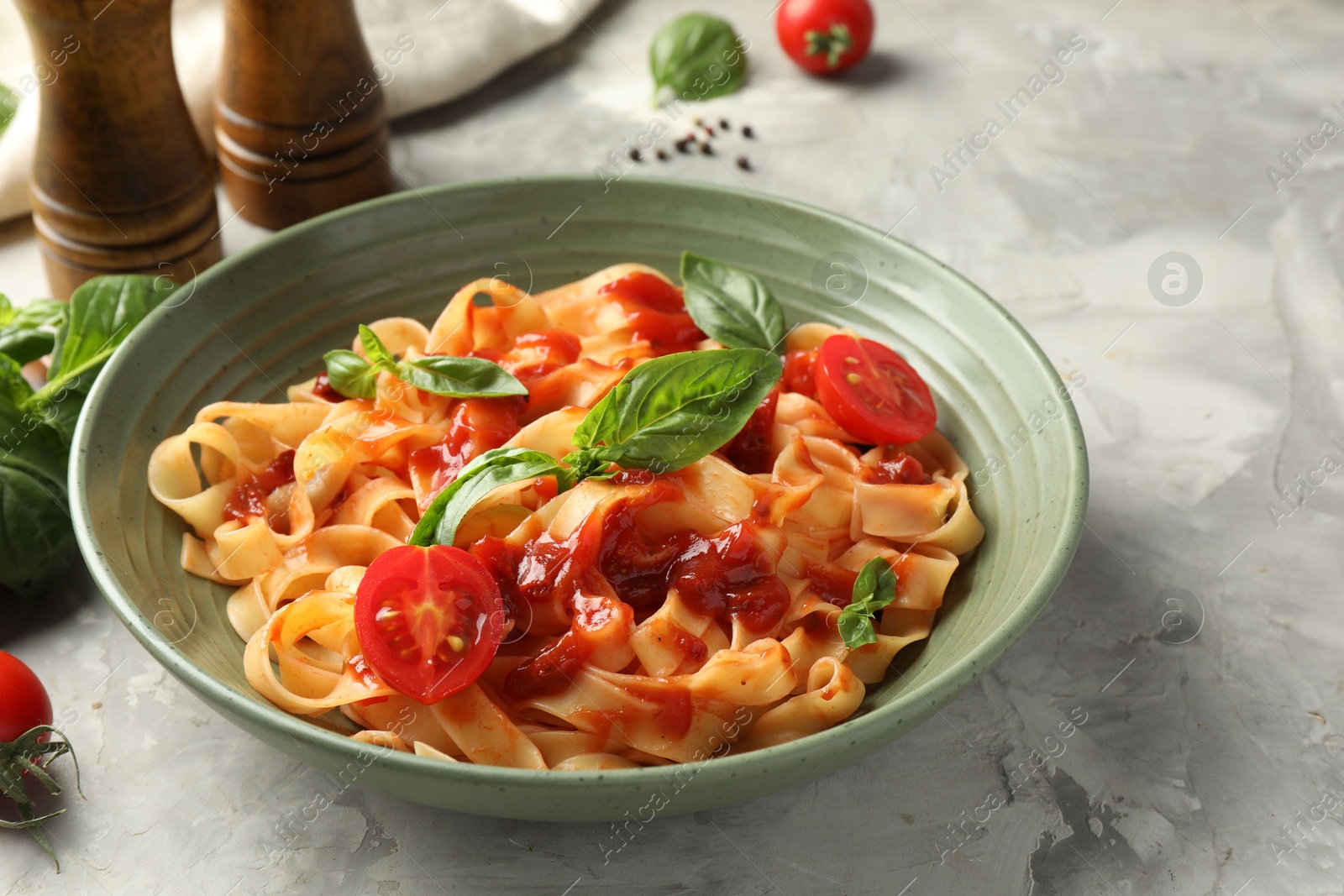 Photo of Delicious pasta with tomato sauce and basil in bowl on grey textured table, closeup