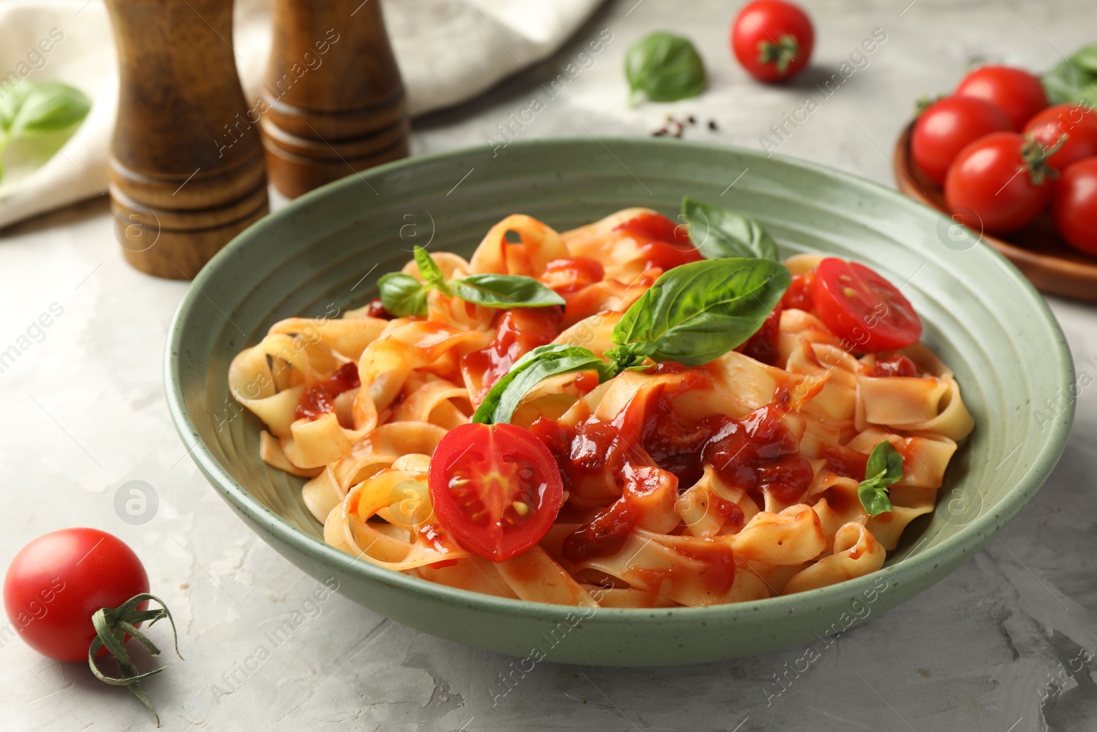 Photo of Delicious pasta with tomato sauce and basil in bowl on grey textured table, closeup