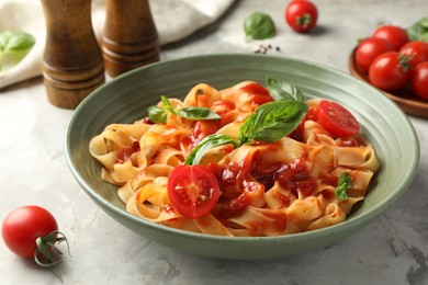 Delicious pasta with tomato sauce and basil in bowl on grey textured table, closeup