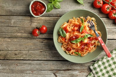 Delicious pasta with tomato sauce, basil, vegetables and fork on wooden table, flat lay. Space for text