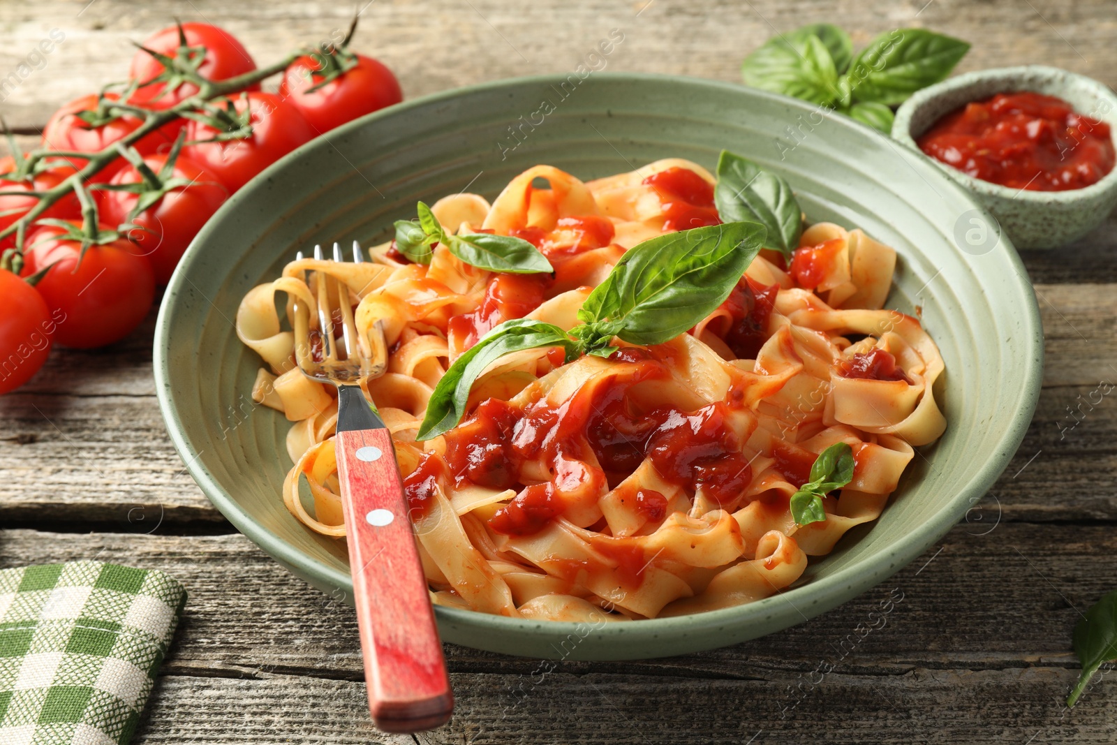 Photo of Delicious pasta with tomato sauce and basil in bowl on wooden table, closeup