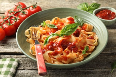 Delicious pasta with tomato sauce and basil in bowl on wooden table, closeup