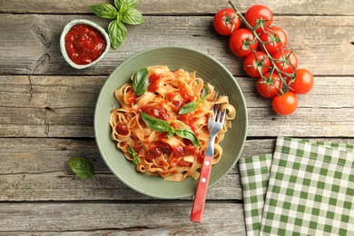 Photo of Delicious pasta with tomato sauce and basil on wooden table, flat lay