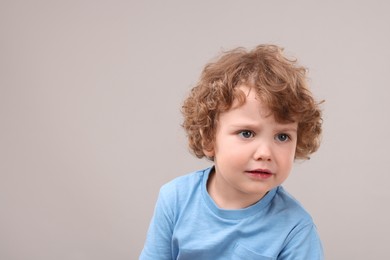 Portrait of cute little boy on grey background, space for text