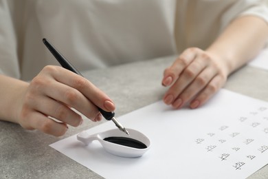 Photo of Calligraphy. Woman dipping fountain pen into inkwell at grey table, closeup