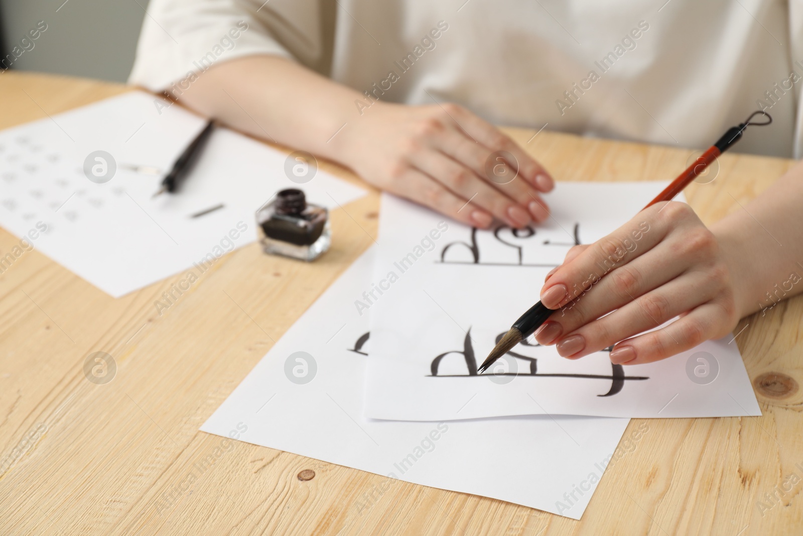 Photo of Calligraphy. Woman with brush writing Hindi letters on paper at wooden table, closeup