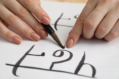 Photo of Calligraphy. Woman with brush writing Hindi letters on paper, closeup