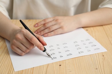 Photo of Calligraphy. Woman with fountain pen writing on paper at wooden table, closeup