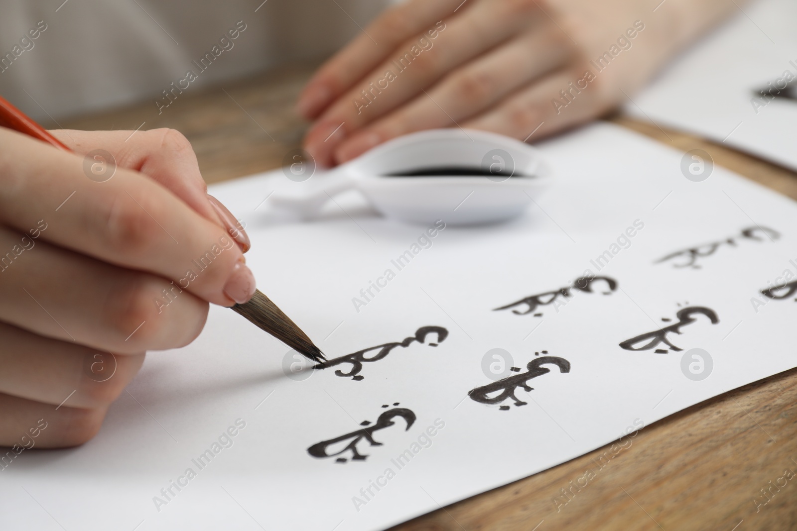 Photo of Calligraphy. Woman with fountain pen writing on paper at wooden table, closeup