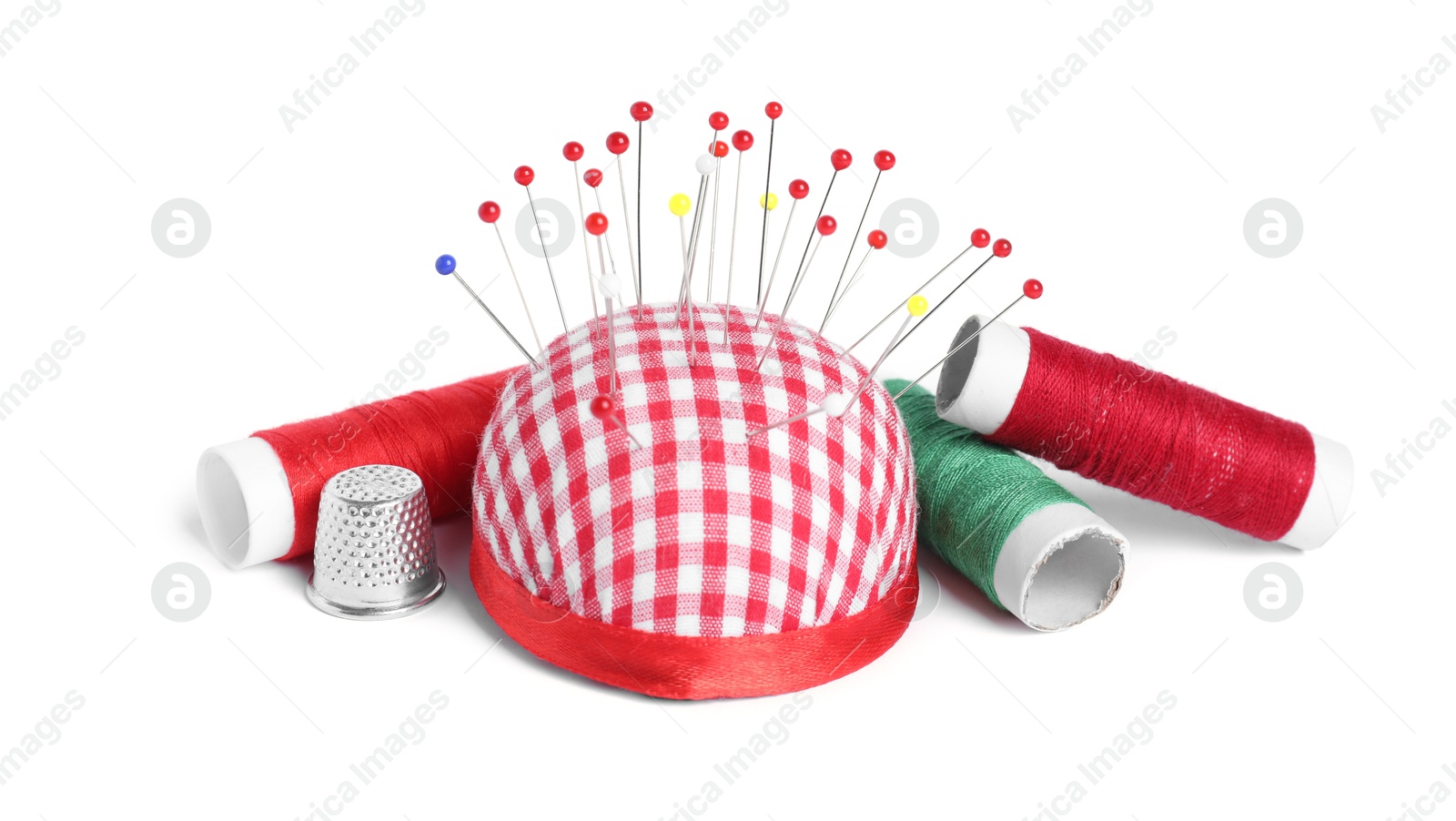 Photo of Checkered pincushion, sewing pins, spools of threads and thimble isolated on white