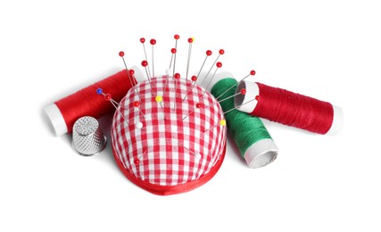 Checkered pincushion, sewing pins, spools of threads and thimble isolated on white