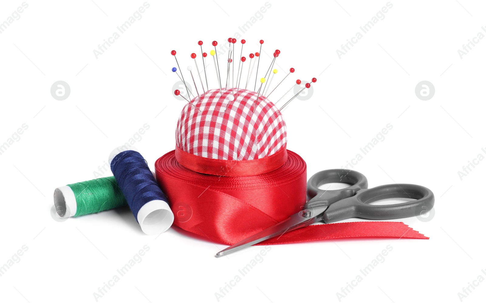 Photo of Checkered pincushion, sewing pins, spools of threads, ribbon and scissors isolated on white