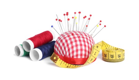 Photo of Checkered pincushion with sewing pins, spools of threads and measuring tape isolated on white