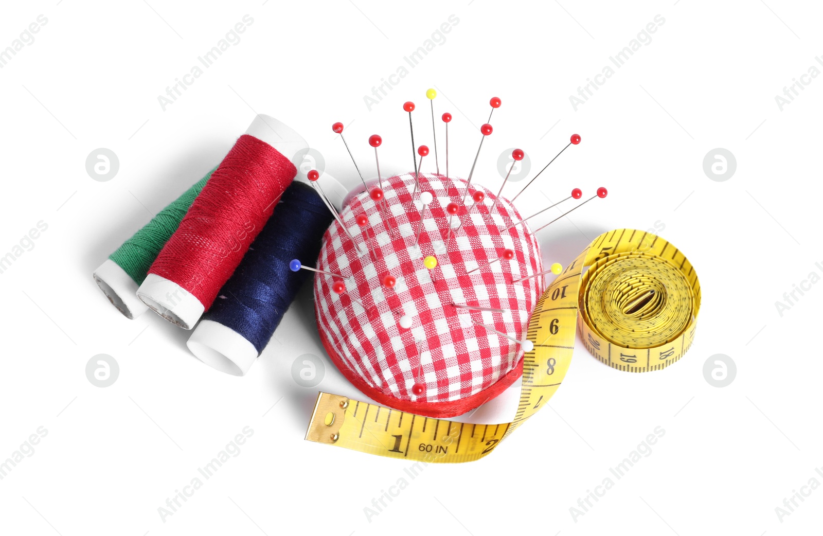 Photo of Checkered pincushion with sewing pins, spools of threads and measuring tape isolated on white, top view