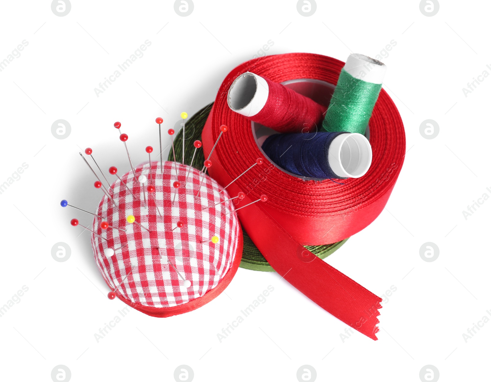 Photo of Checkered pincushion with sewing pins, spools of threads and ribbons isolated on white, top view