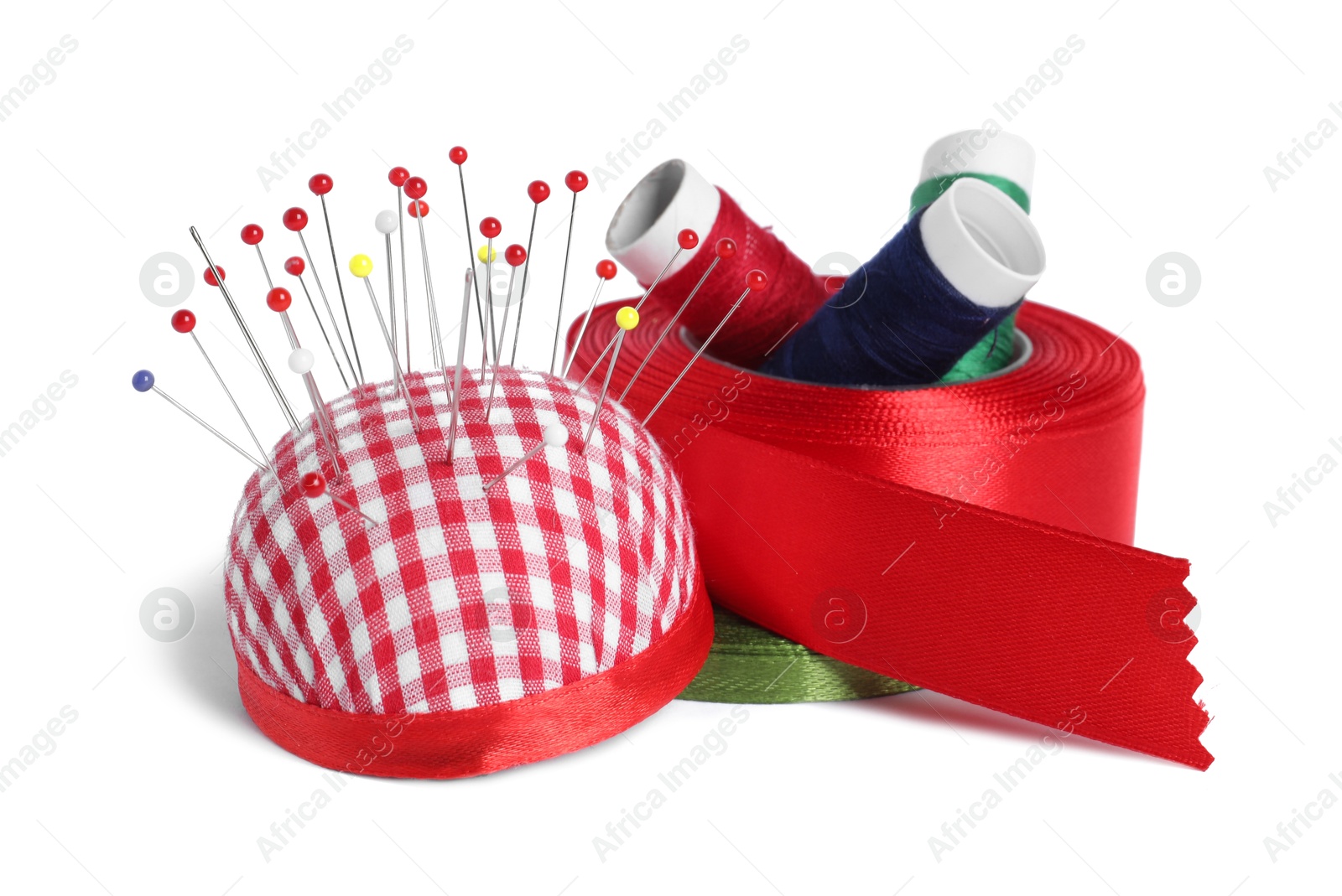 Photo of Checkered pincushion with sewing pins, spools of threads and ribbons isolated on white