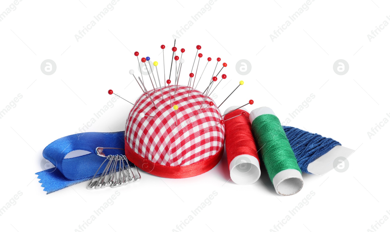Photo of Checkered pincushion with sewing pins, spools of threads and ribbon isolated on white
