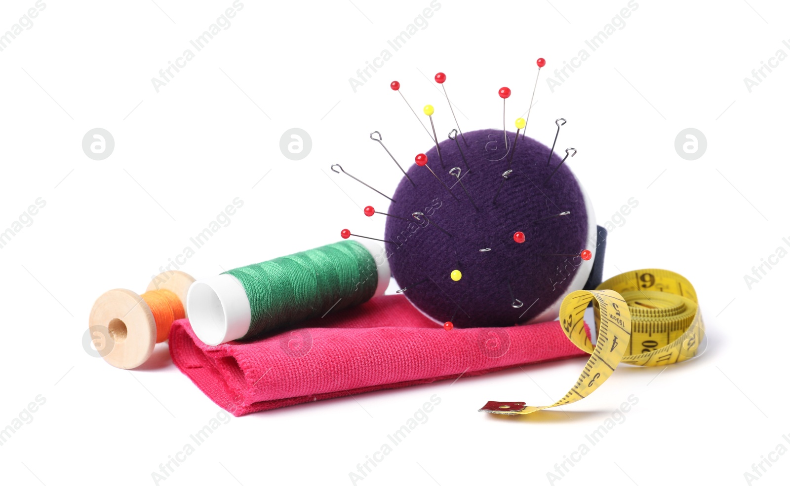 Photo of Blue pincushion with sewing needles, spools of threads, measuring tape and cloth isolated on white