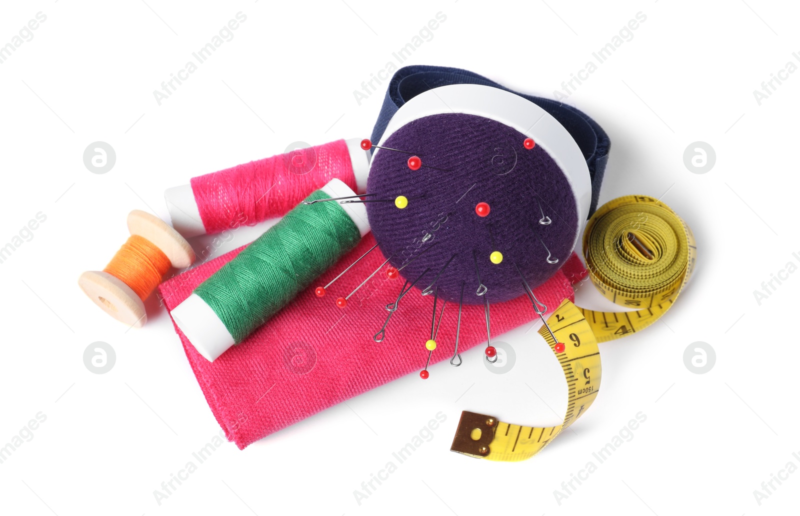 Photo of Blue pincushion with sewing needles, spools of threads, measuring tape and cloth isolated on white, above view